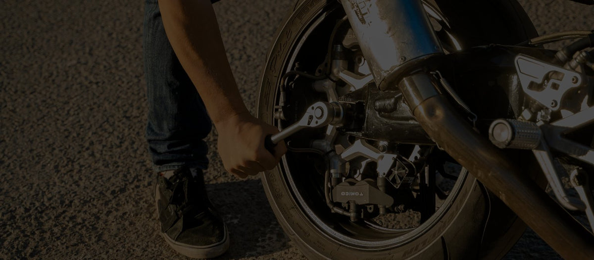 Rider tightening a motorcycle rear wheel with a ratchet